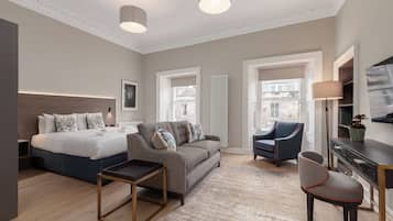 Quarto de hotel moderno com cama, sofá, poltrona e uma pequena mesa.