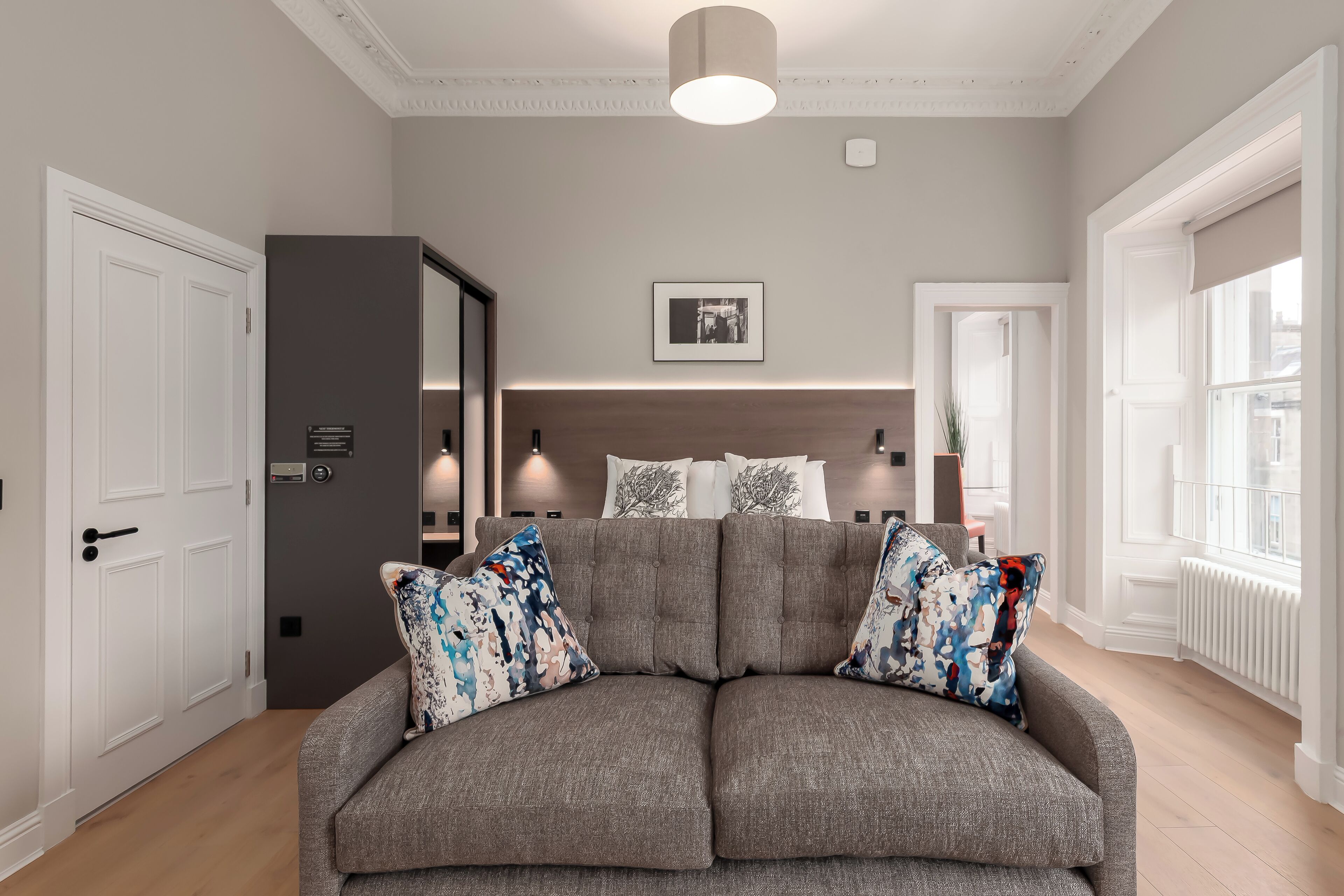 A modern living room with a grey sofa, white doors, and a framed picture on the wall.
