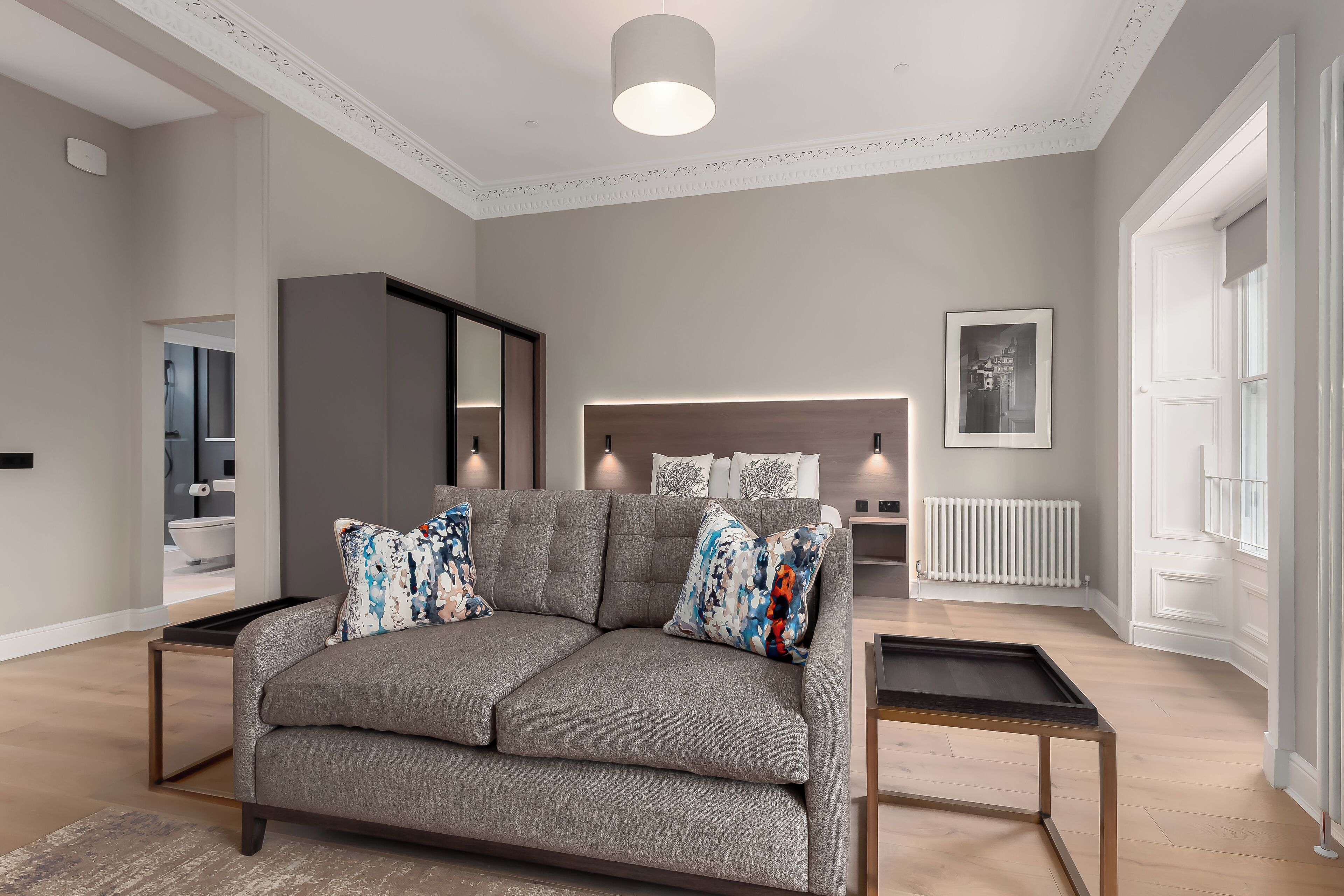 A modern living room with a grey sofa, two side tables, a radiator, and a framed picture on the wall.