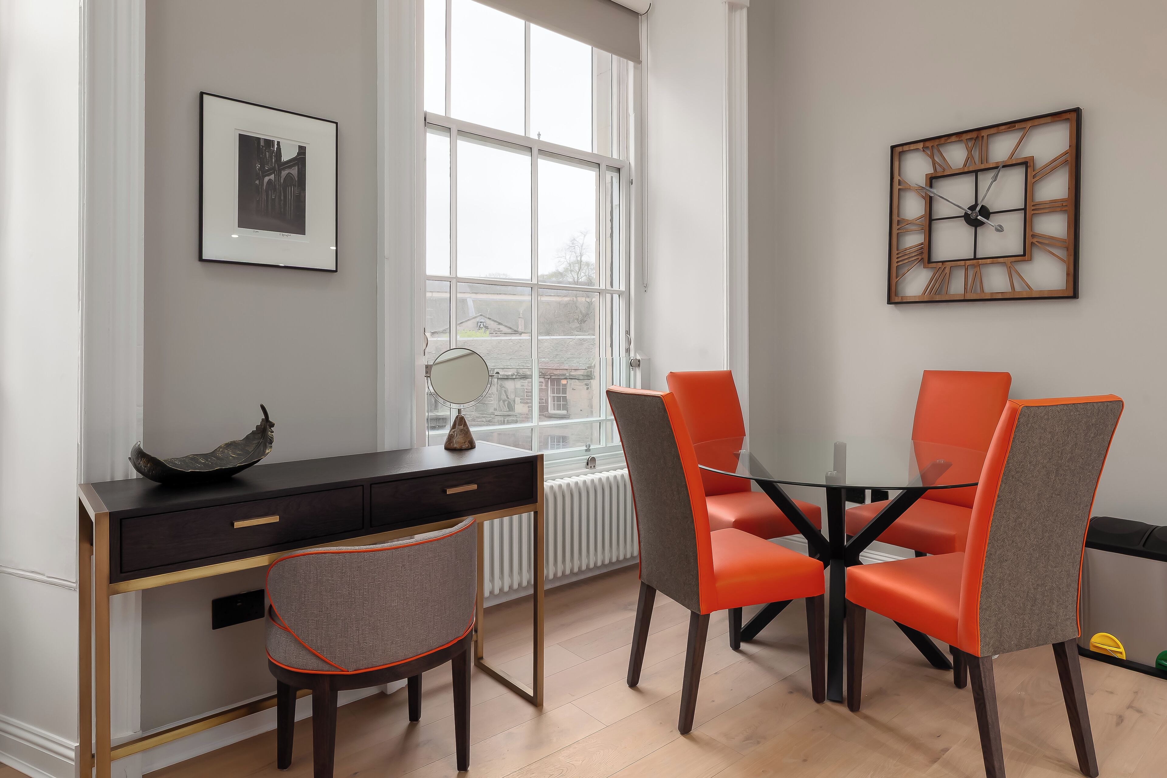 Una habitación moderna con escritorio, dos sillas, un cuadro enmarcado y un ventanal grande.