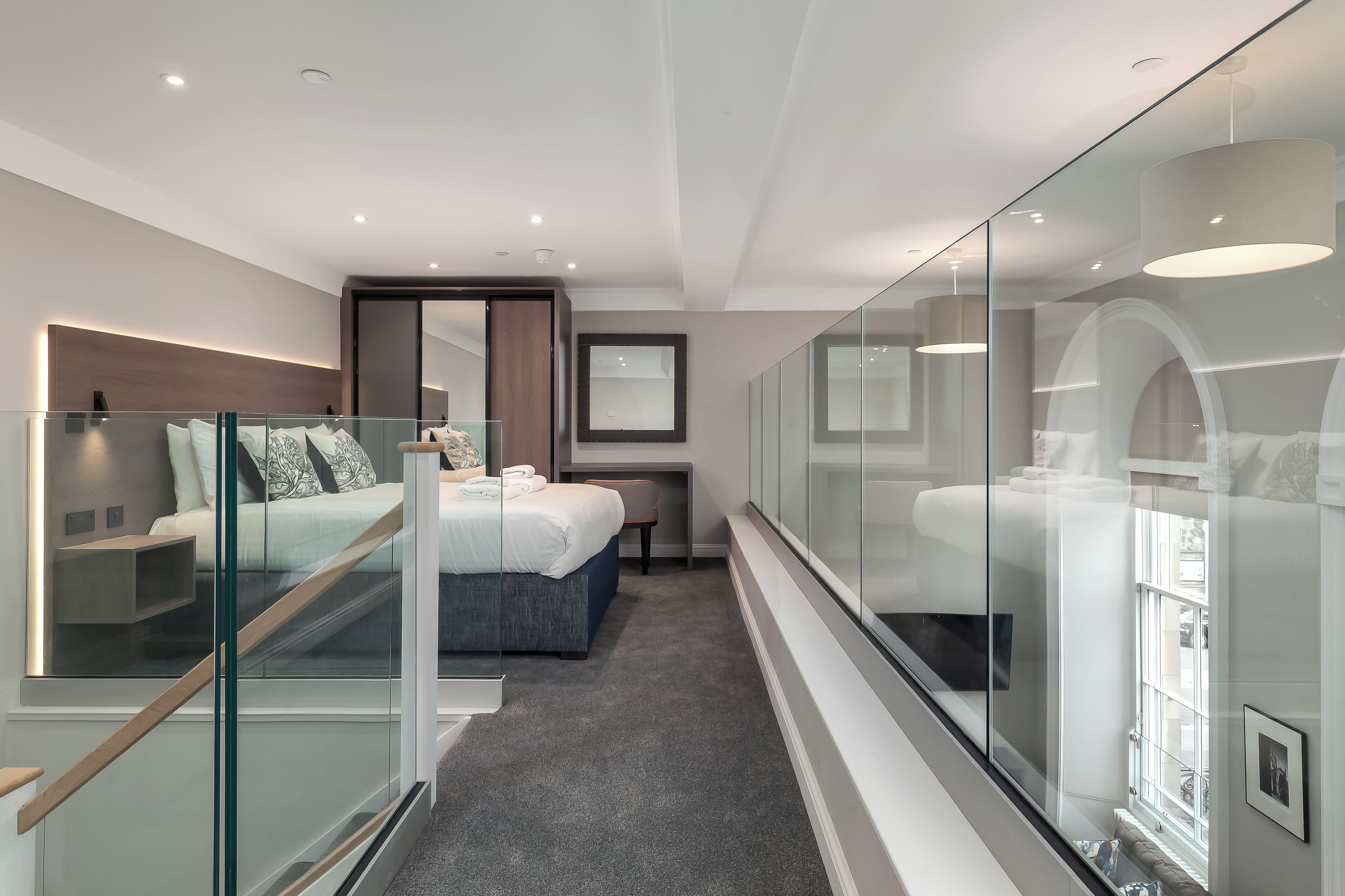 Une chambre d’hôtel moderne dotée d’une paroi en verre, d’un lit, d’un bureau et offrant une vue sur la ville par la fenêtre.