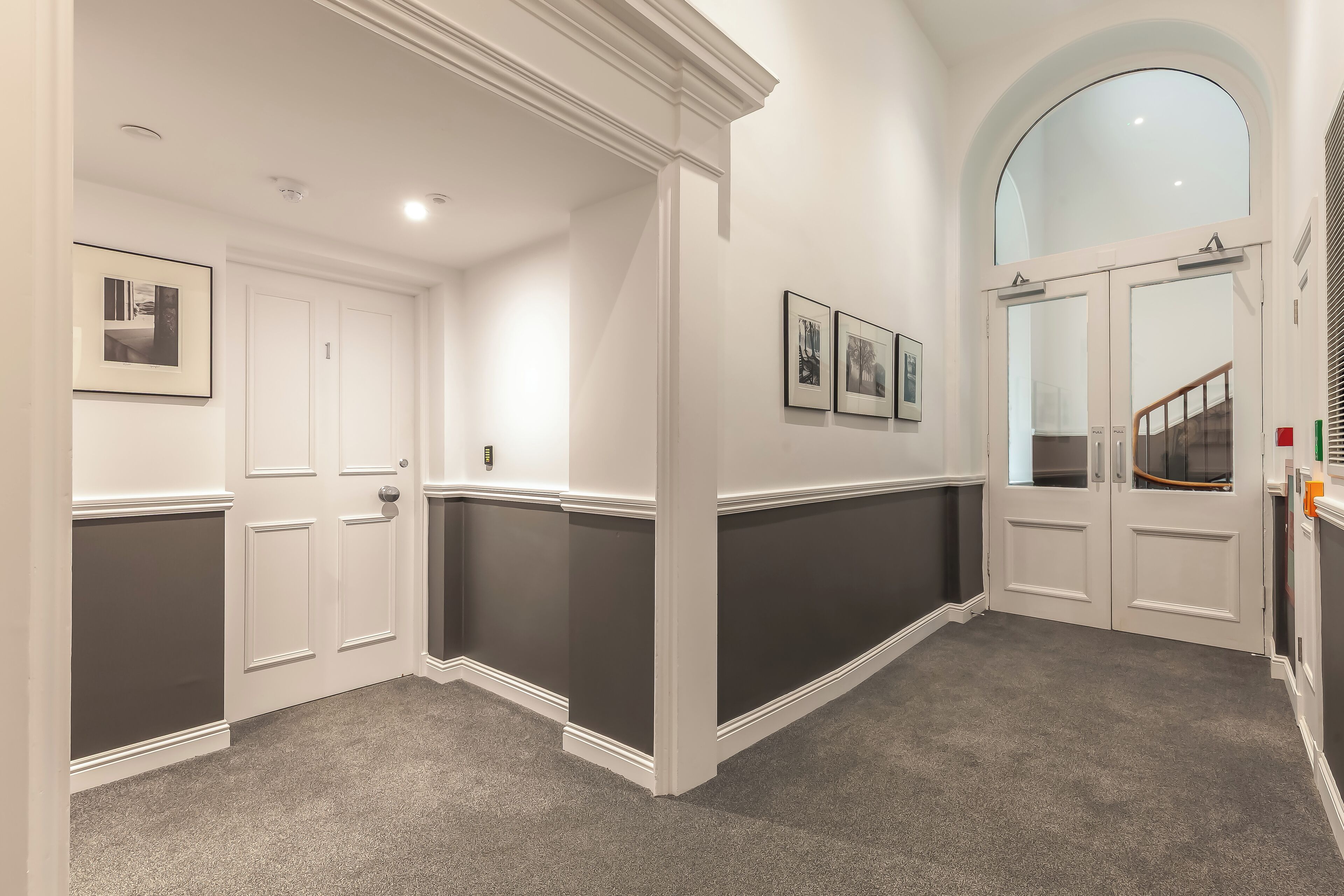 A hallway with dark and light wall panels, white doors, and framed pictures on the walls.