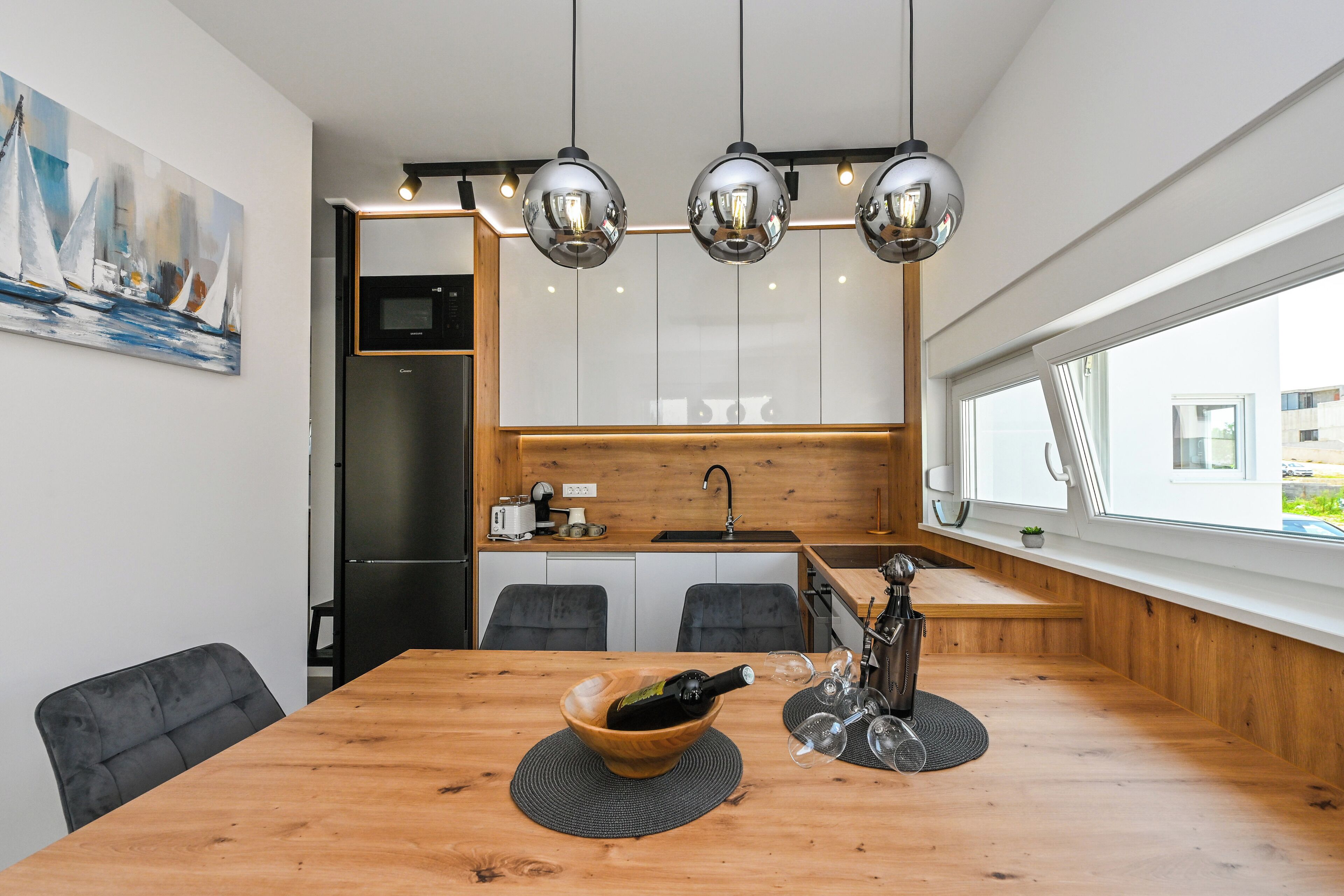 Une cuisine moderne avec des meubles blancs, un plan de travail en bois et un coin repas doté d’une table en bois.