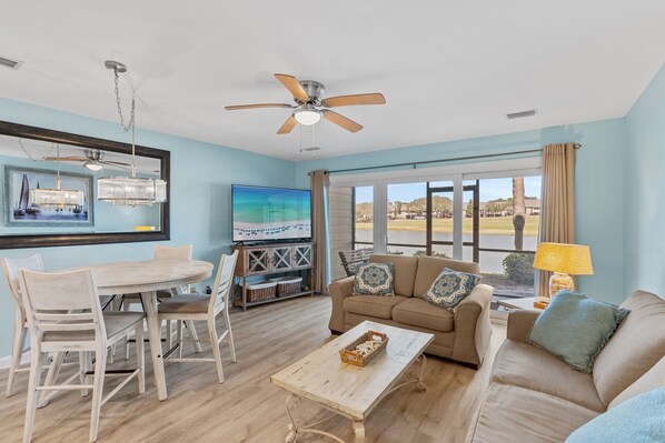A spacious living room with a ceiling fan, a dining table with chairs, a sofa, and a TV. - Ground Floor Seascape Resort Villa! 50 Steps to BEACH! Pool, Tennis, Shopping (Miramar Beach)