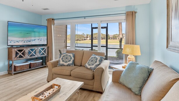 Una sala de estar con un sofá color beige, un televisor y vista a un lago.