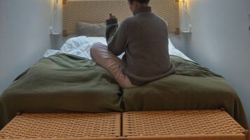 Ein Zimmer mit Oberlicht, einem Bett mit grüner Bettdecke, einer gewebten Bank und zwei Wandlampen.