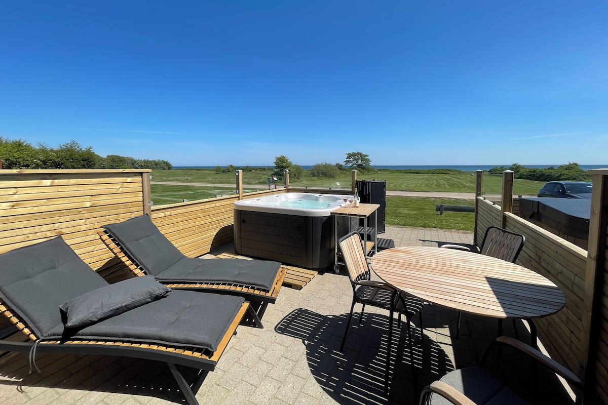 An outdoor patio with lounge chairs, a hot tub, and a table with chairs.