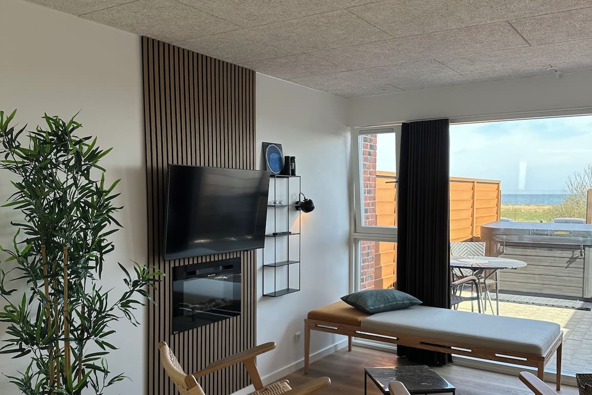 A modern living room with a TV, wooden furniture, a large plant, and a view of the outdoors.