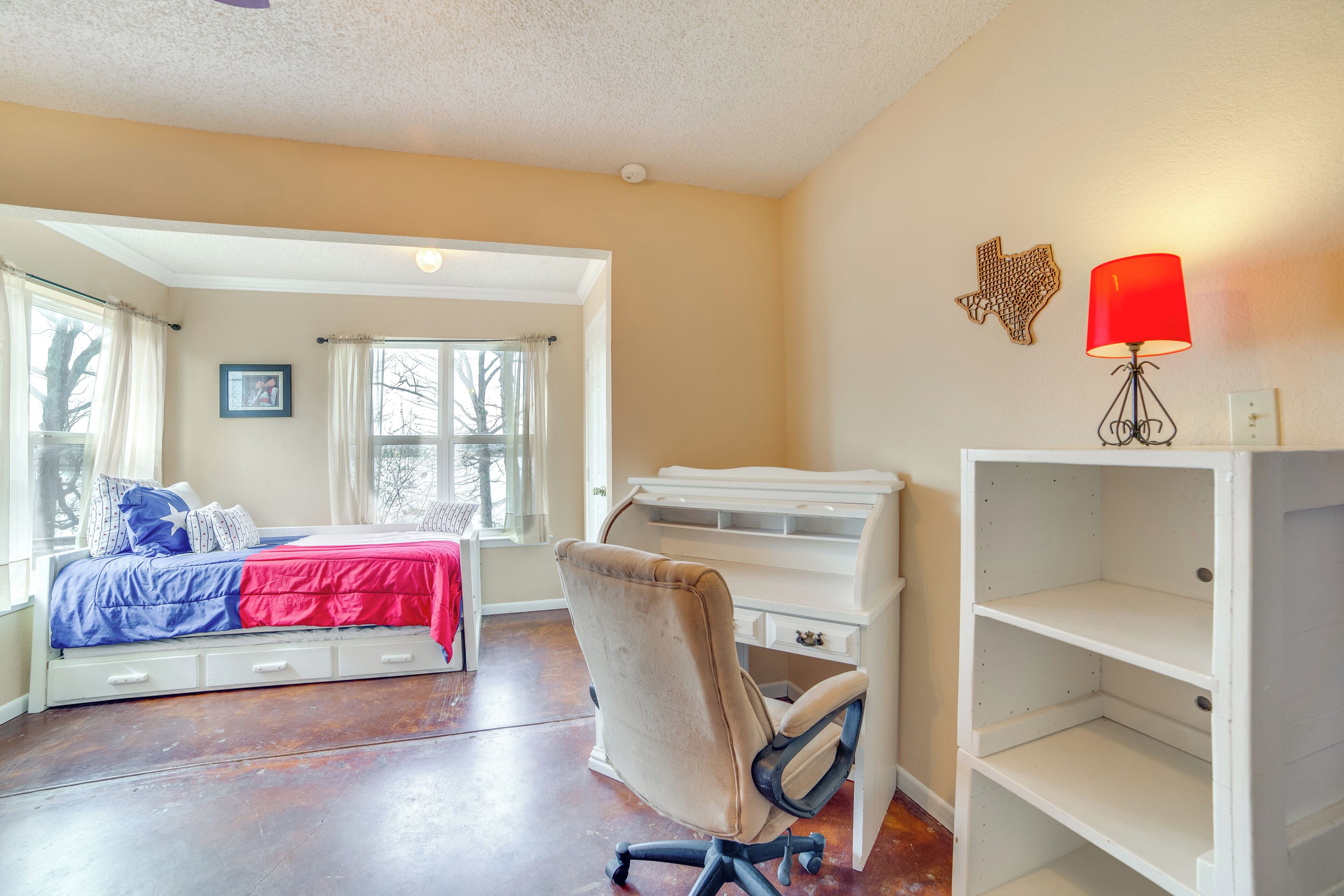 A bedroom with a bed, desk, chair, and a red lamp.