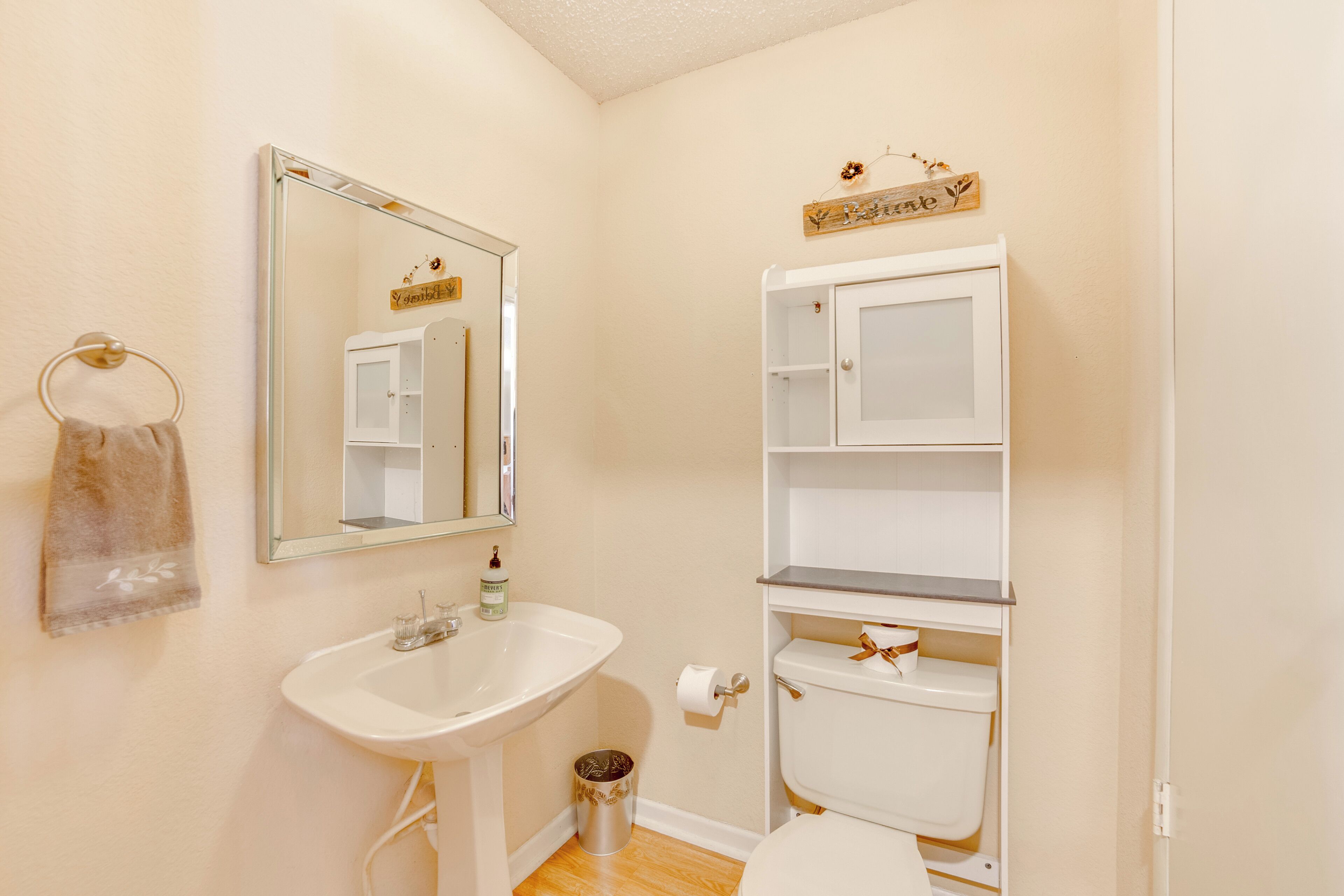 A bathroom with a sink, mirror, toilet, and storage shelves.