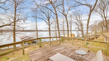 Relax on the deck overlooking the serene lake, surrounded by bare trees and a wooden railing.