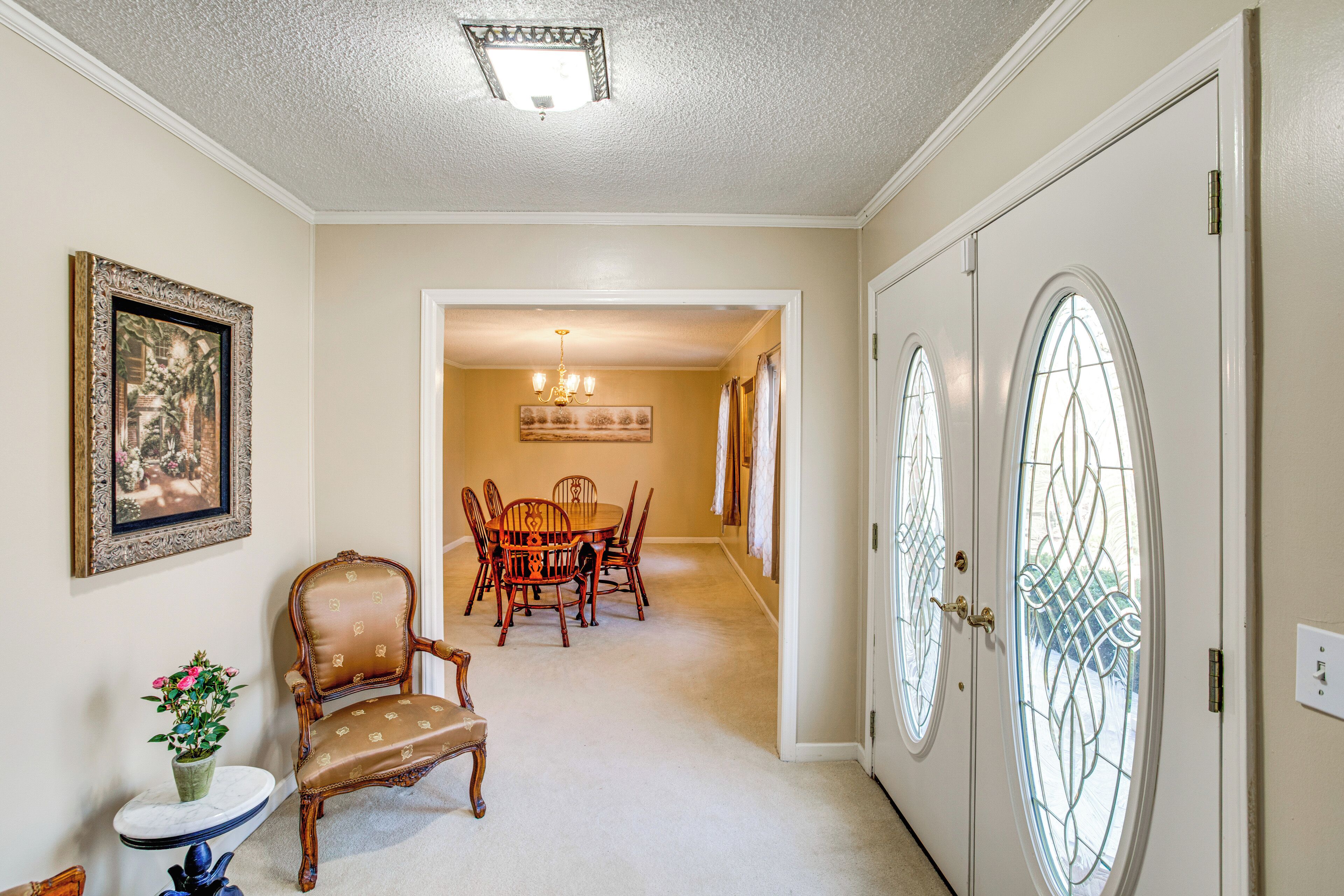 A hallway with a dining area, a chair, a table, and a door with a glass window.