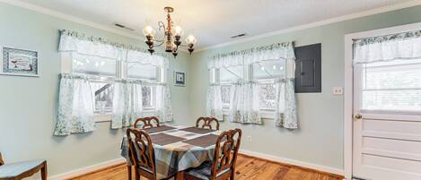 A dining room with a wooden table, four chairs, a chandelier, and floral curtains.
