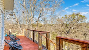Une terrasse en bois avec une balustrade, deux fauteuils à bascule et une vue sur les arbres et les collines.