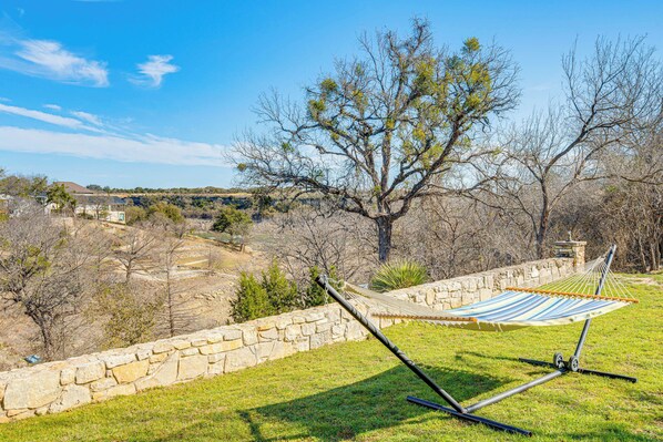 A hammock in a grassy area with a stone wall and a tree in the background. - Hill Country Retreat w/ Lake View, Deck & Balcony (Spicewood)