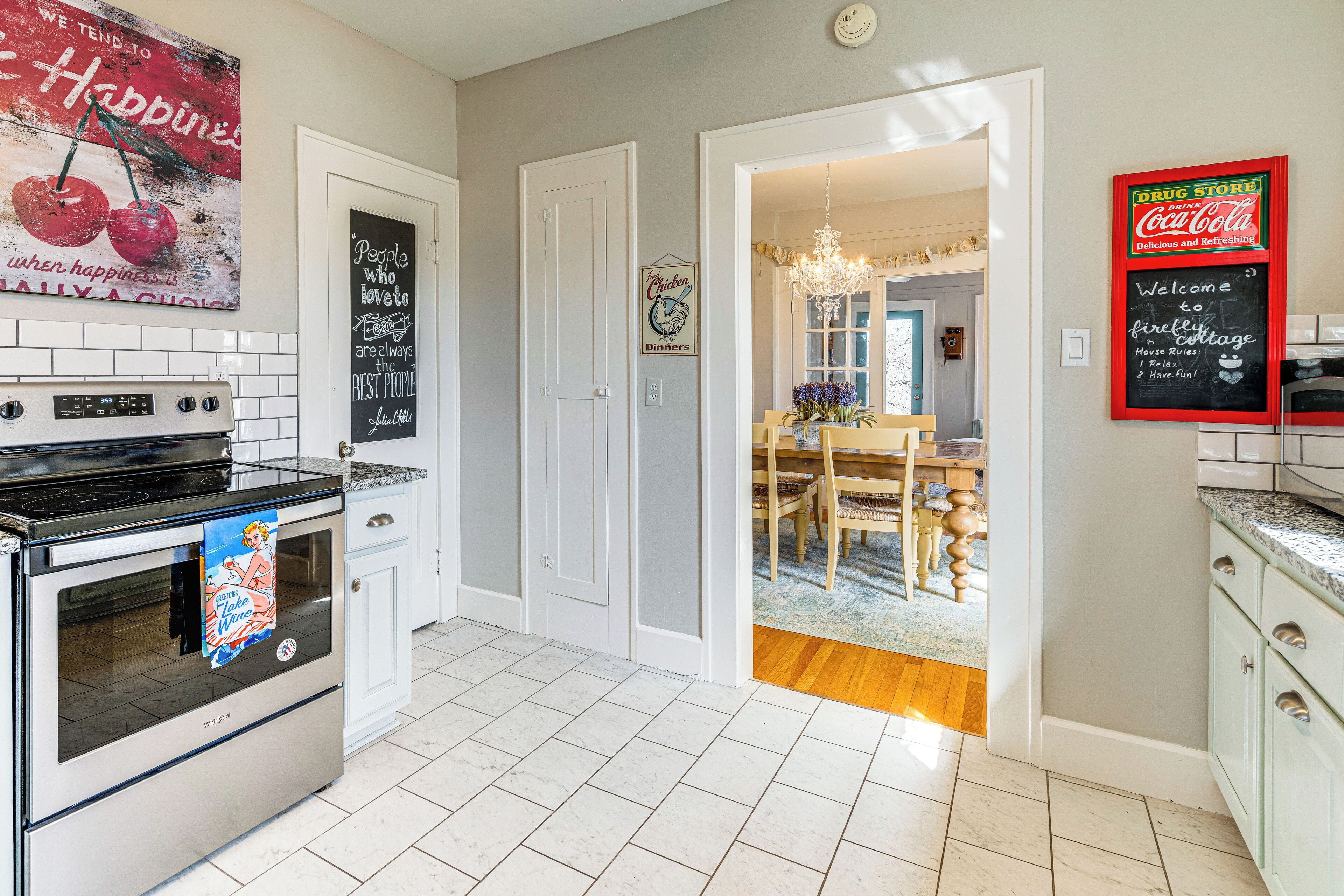 A kitchen with white cabinets, a stainless steel oven, and a tiled floor. There is a sign on the wall advertising a drug store and Coca-Cola.