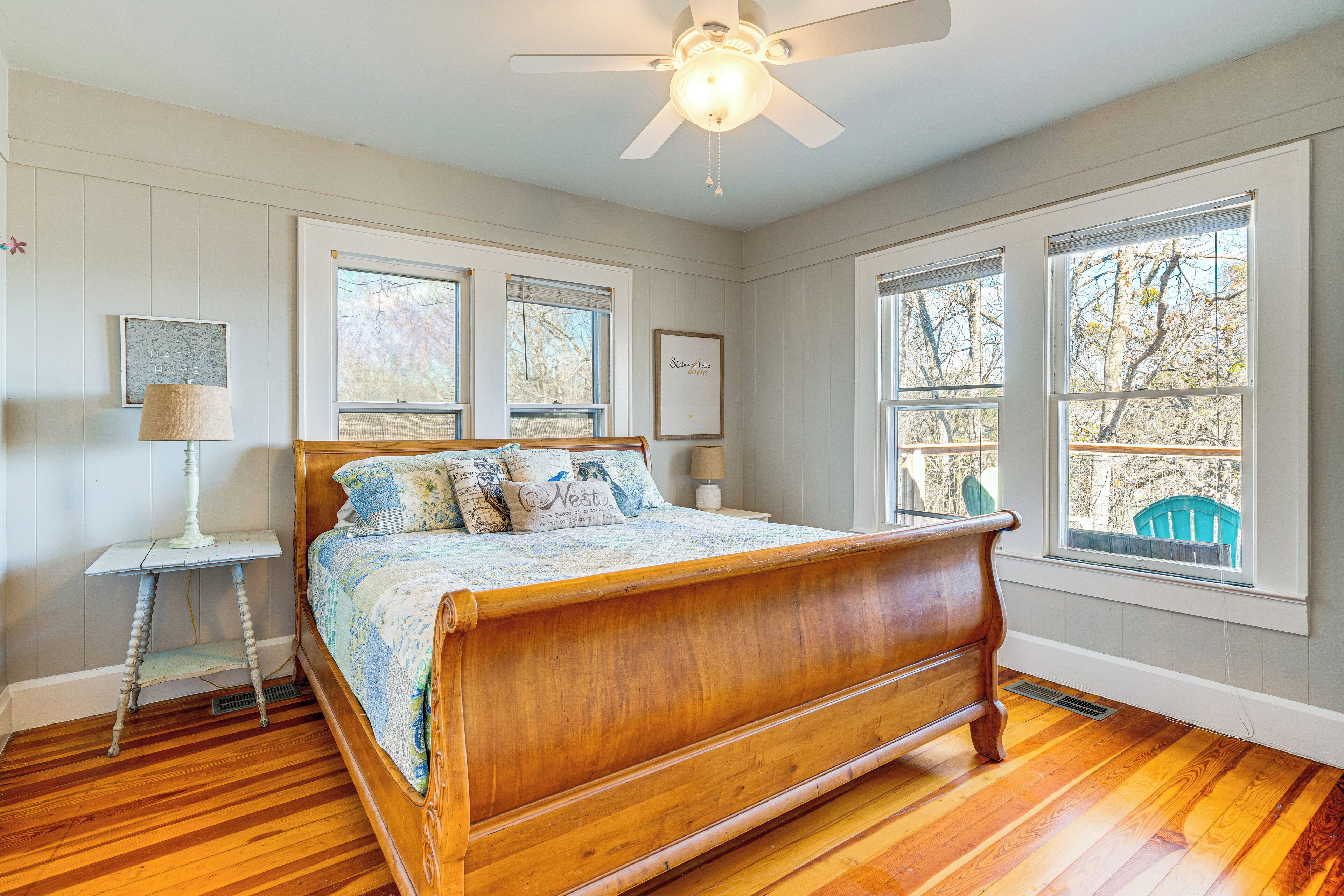 A bedroom with a wooden bed, a ceiling fan, and large windows with a view of the outdoors.