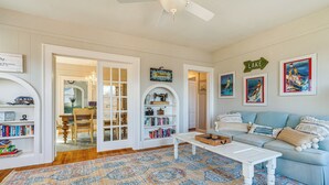 Un salon avec un canapé blanc, une table basse, un tapis à motifs et une bibliothèque remplie de livres et d’objets décoratifs.