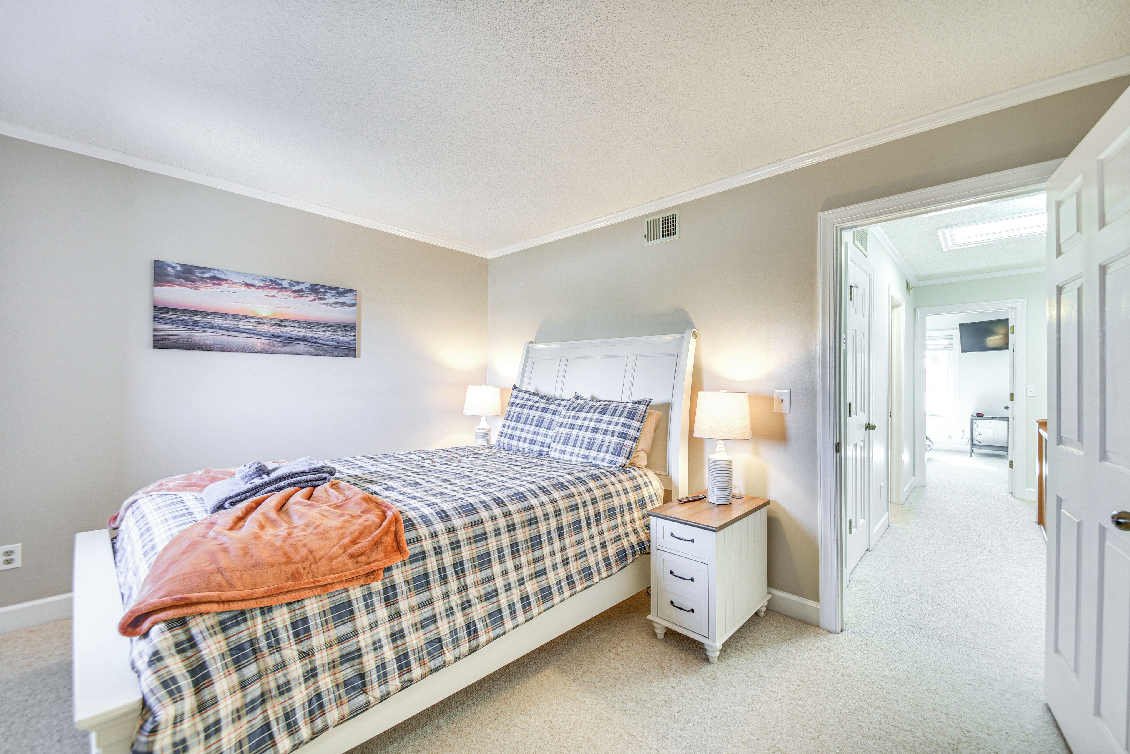 A bedroom with a bed, nightstands, a painting, and a hallway leading to another room.