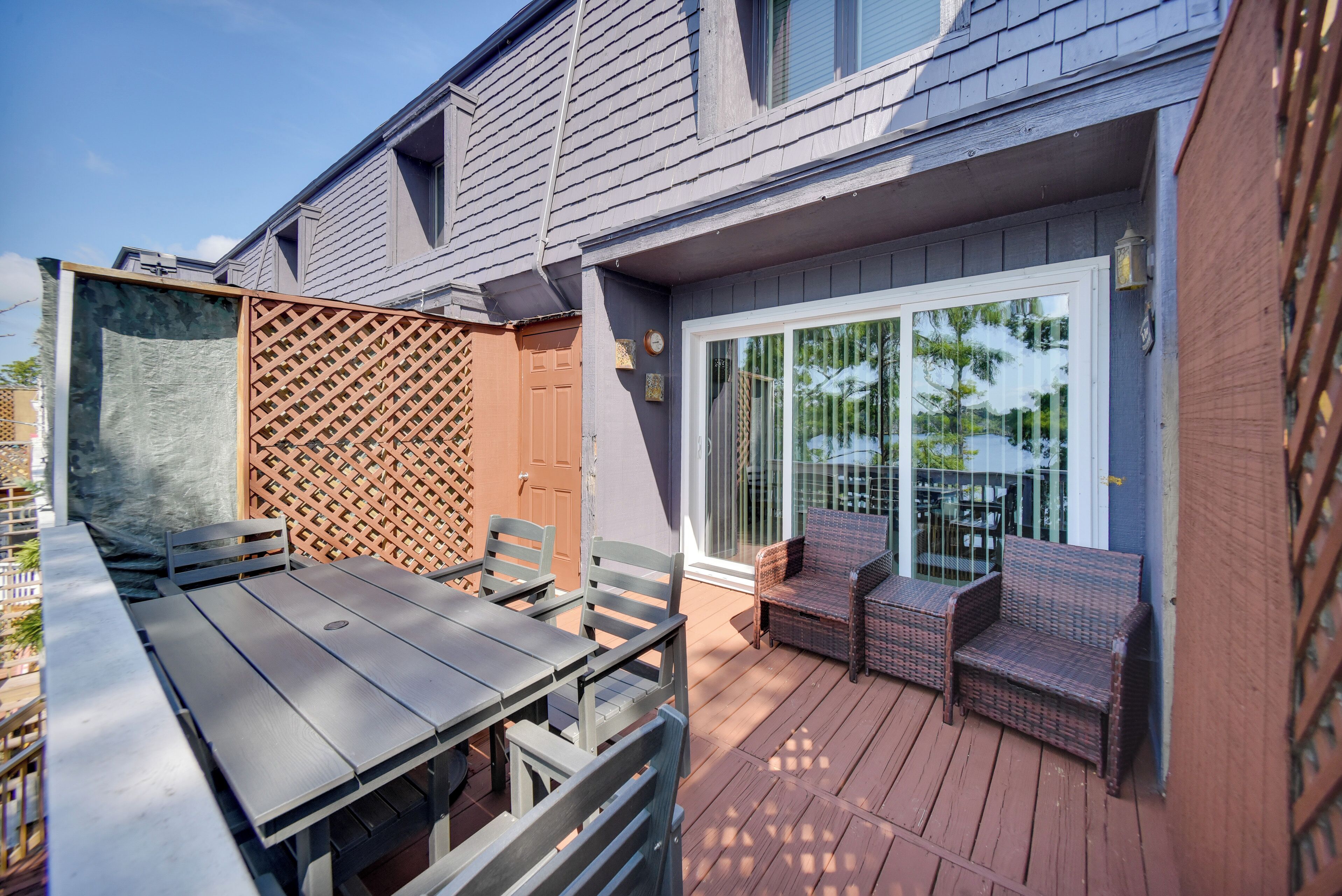 A patio with a wooden table and chairs, a wicker sofa, and a sliding glass door leading to a covered area.
