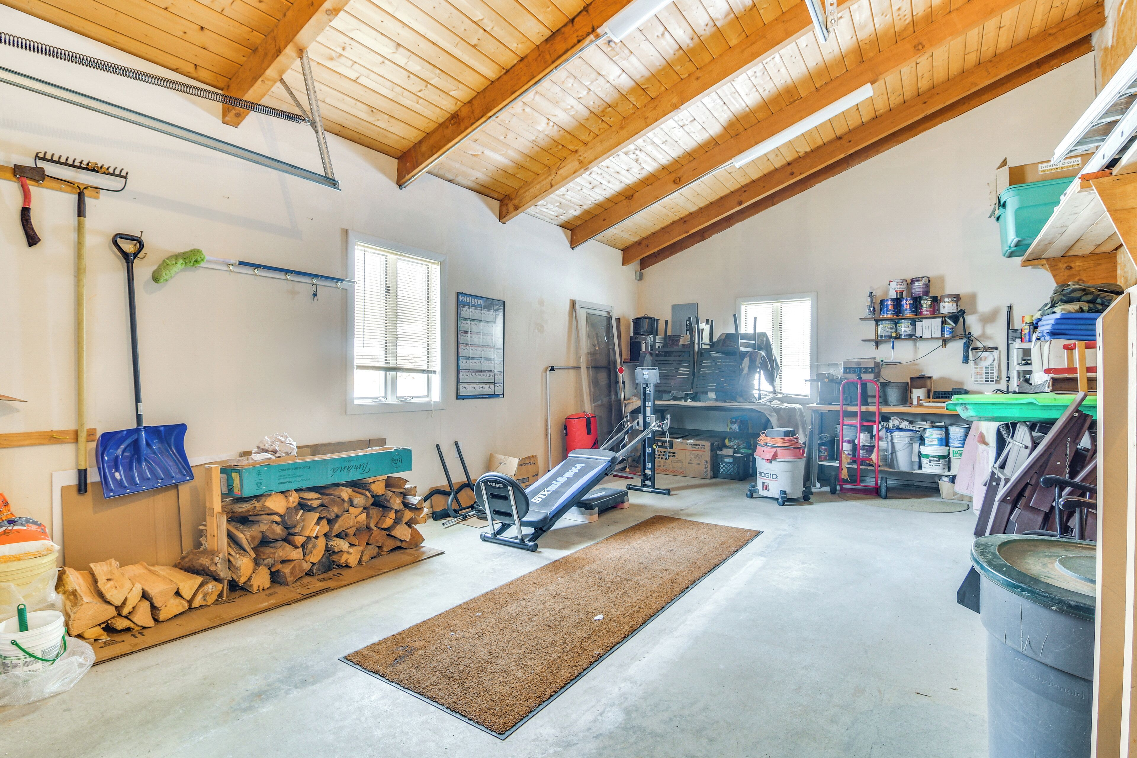 A spacious attic room with a wooden ceiling, exercise equipment, a large window, and various storage items.