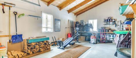 A spacious attic room with a wooden ceiling, exercise equipment, a large window, and various storage items.