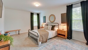 Een slaapkamer met een bed, nachtkastjes, een bankje, een spiegel en een raam met gordijnen.