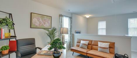 A modern living room with a wooden dining table, a black office chair, a brown leather sofa, and a potted plant.