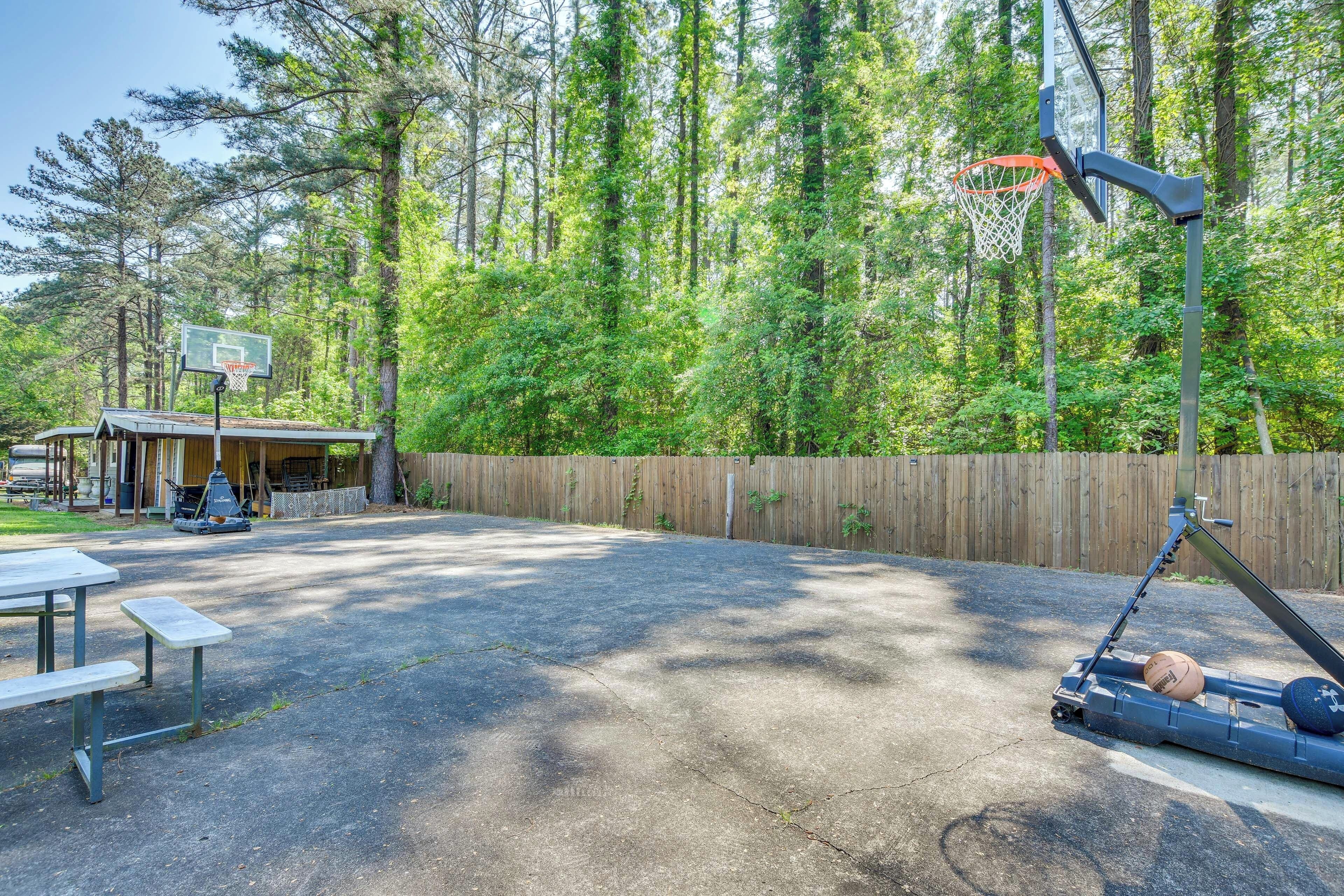 An outdoor basketball court with a wooden fence, picnic tables, and a basketball hoop.