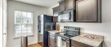 A kitchen with stainless steel appliances, wooden cabinets, and a window with blinds.