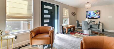 A modern living room with leather sofas, a glass coffee table, and a dining area with a TV and seating.