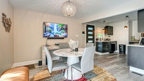 Una cocina moderna con armarios oscuros, un comedor con mesa de mármol y un televisor grande en la pared.