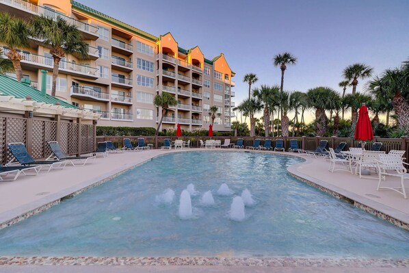 A pool area with lounge chairs and a building with balconies in the background. - Oceanfront beach villa in Palmetto Dunes (Hilton Head)