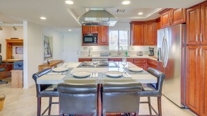 A modern kitchen with wooden cabinets, a stainless steel refrigerator, and a dining area with a table set for four. - Spacious Condo w/ Mtn Views in Palm Desert! (Palm Desert)