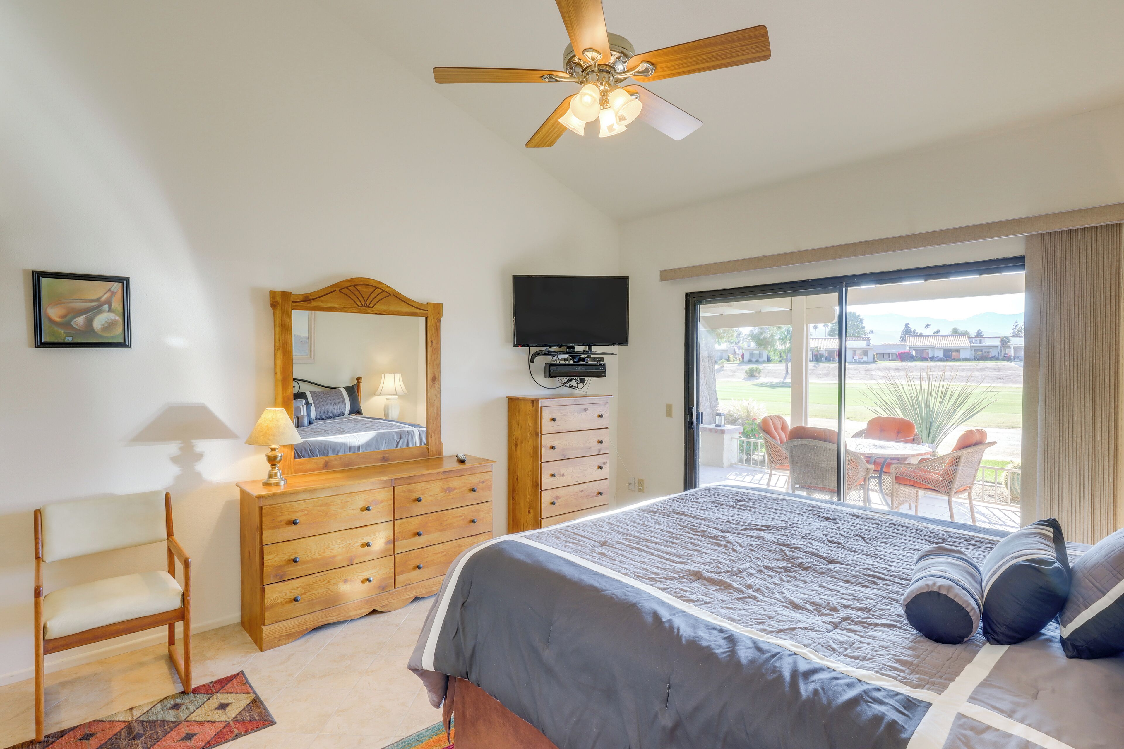 A bedroom with a bed, dresser, TV, and a balcony with outdoor furniture.