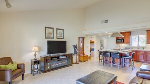 A spacious living room with a flat-screen TV, leather sofas, a coffee table, and a kitchen area with bar stools and a microwave. - Spacious Condo w/ Mtn Views in Palm Desert! (Palm Desert)