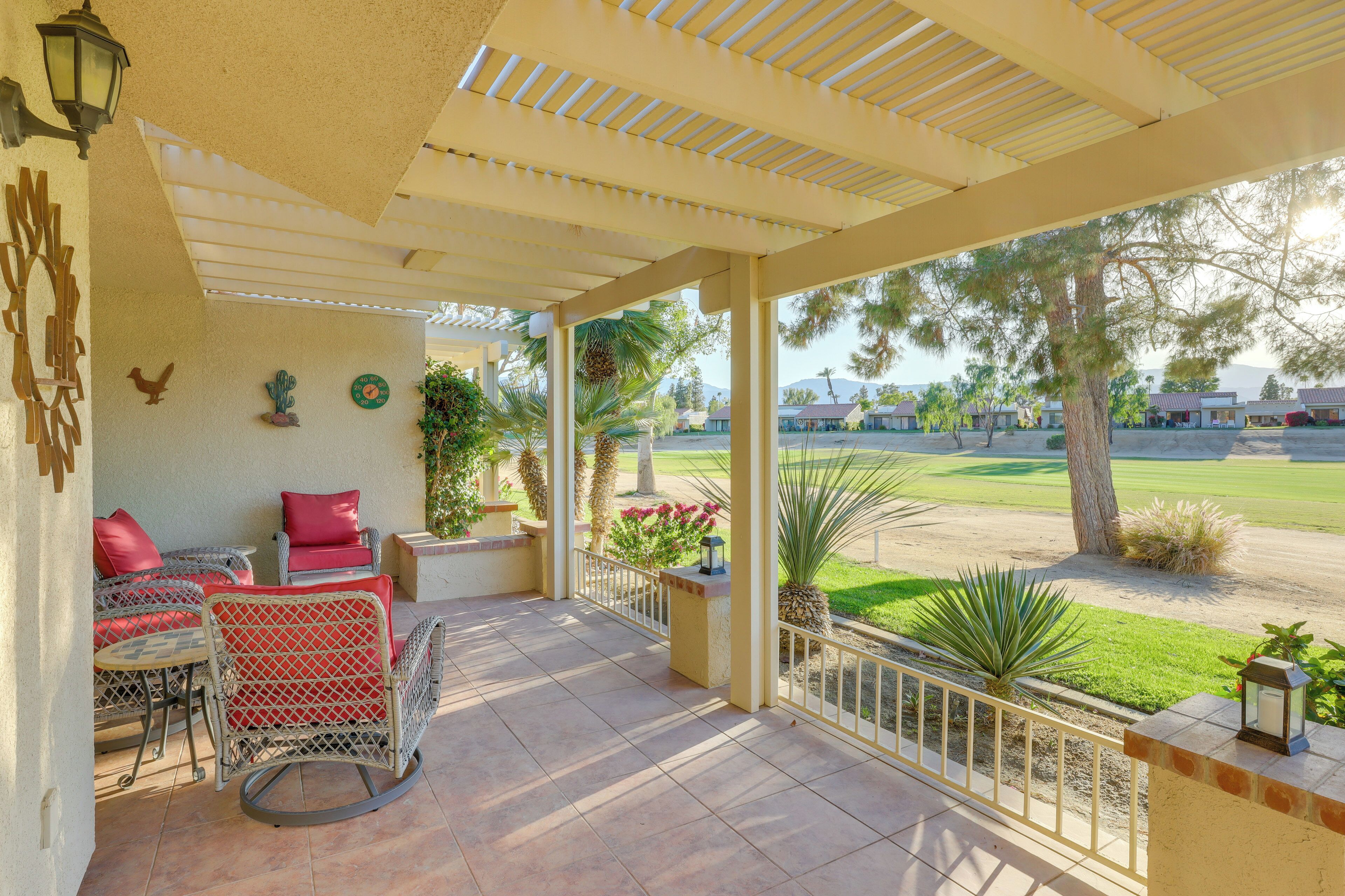 A covered patio with wicker furniture, a view of a golf course, and a desert landscape.