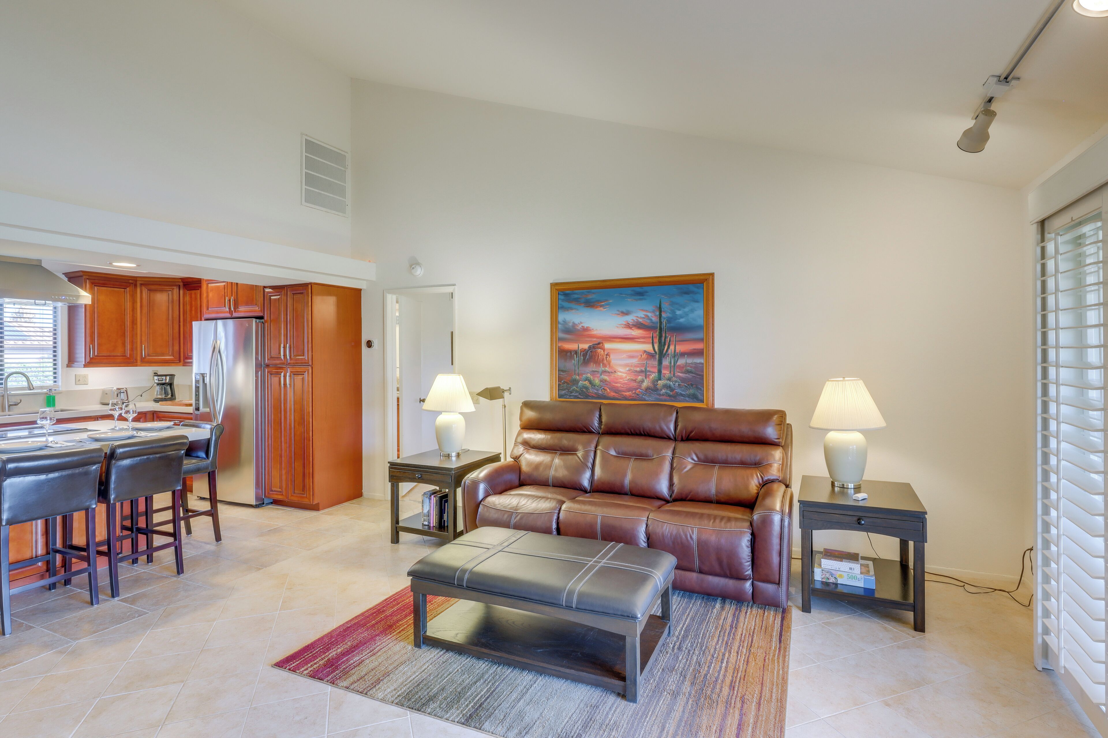A modern living room with a leather sofa, a dining area with a kitchen in the background, and a painting on the wall.