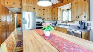 A kitchen with wooden cabinets, a stainless steel refrigerator, a wooden dining table with a patterned table runner, and a hanging pendant light. - Family Mountain Getaway, Retreat to the Cool Pine (Prescott)