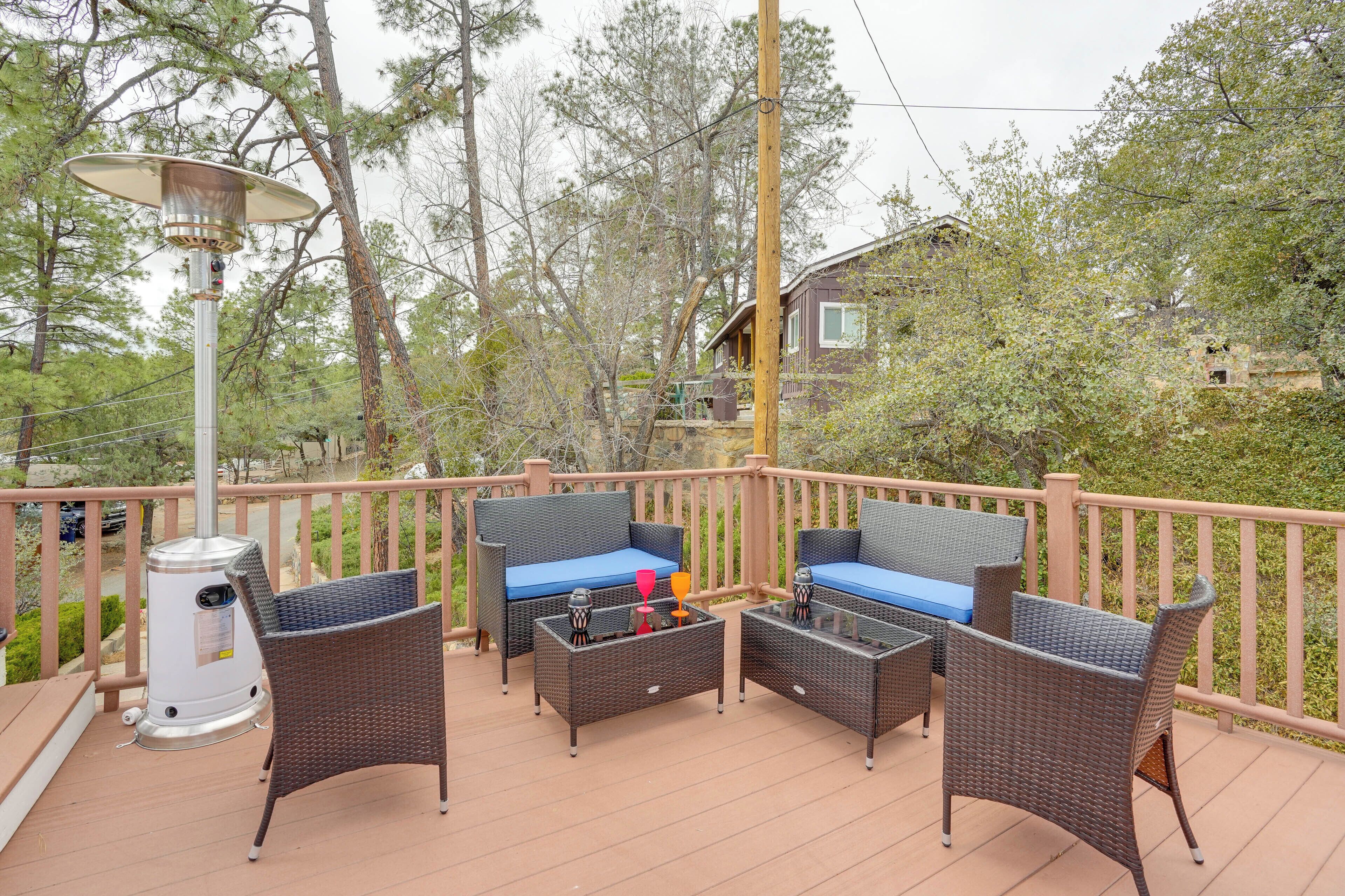 A deck with wicker furniture, a heater, and a view of trees and a house.