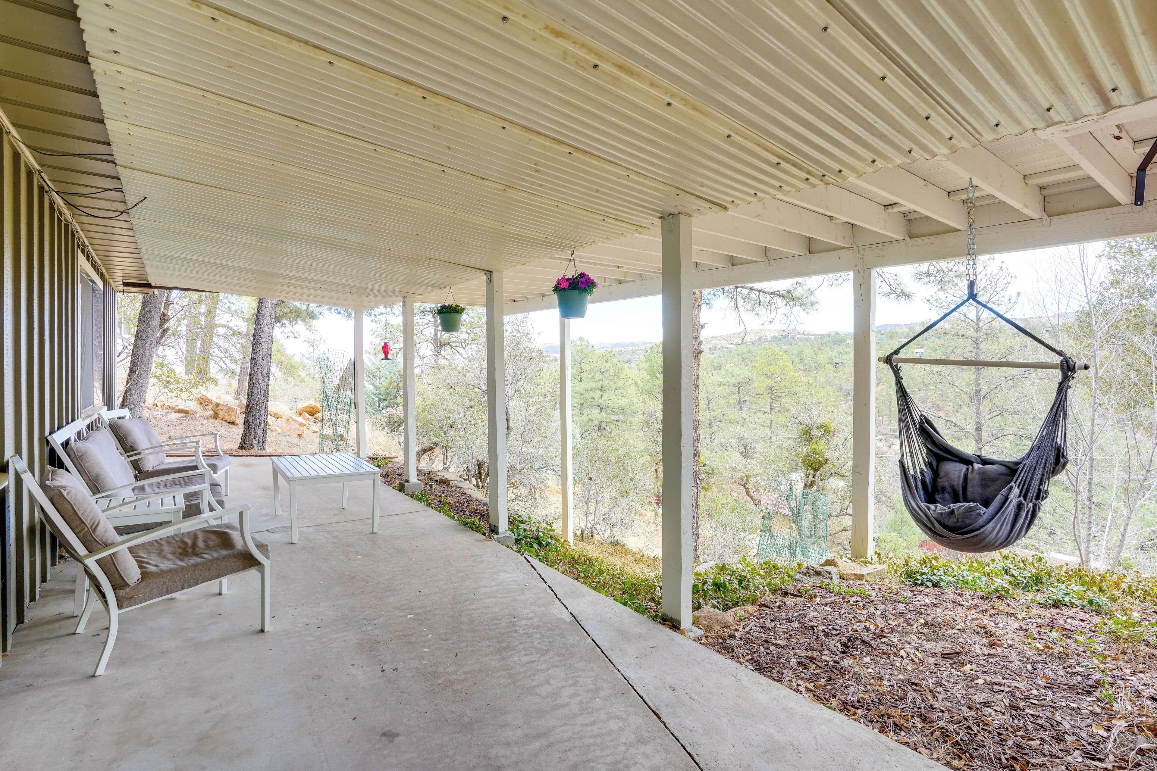 A covered patio with outdoor furniture, a hanging chair, and hanging planters.