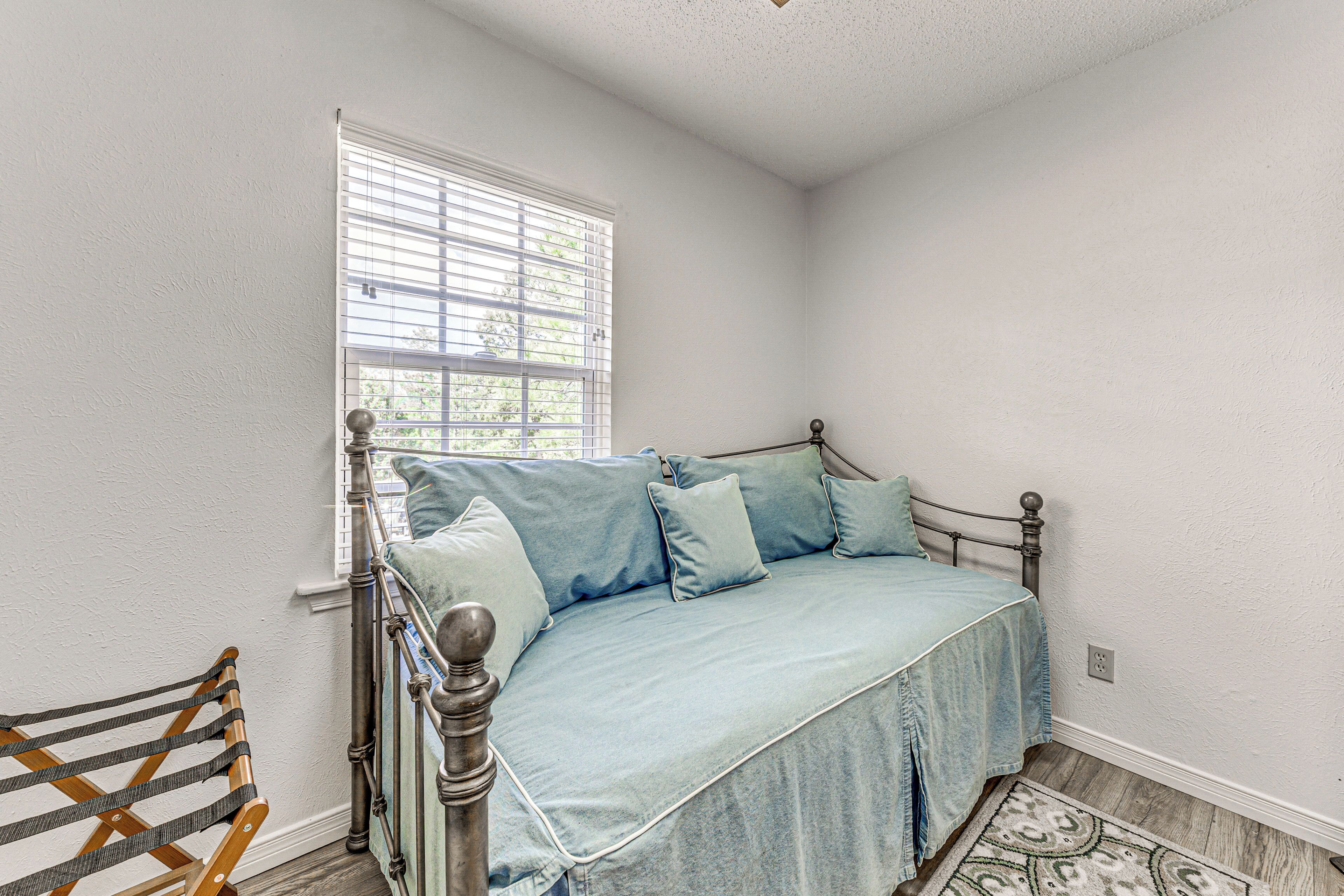 A bedroom with a bed, a window with blinds, a wooden chair, and a patterned rug.