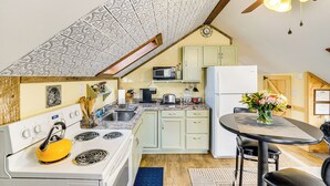 Una cucina compatta con fornello, microonde e frigorifero, un tavolo da pranzo con sedie e una ventola a soffitto.