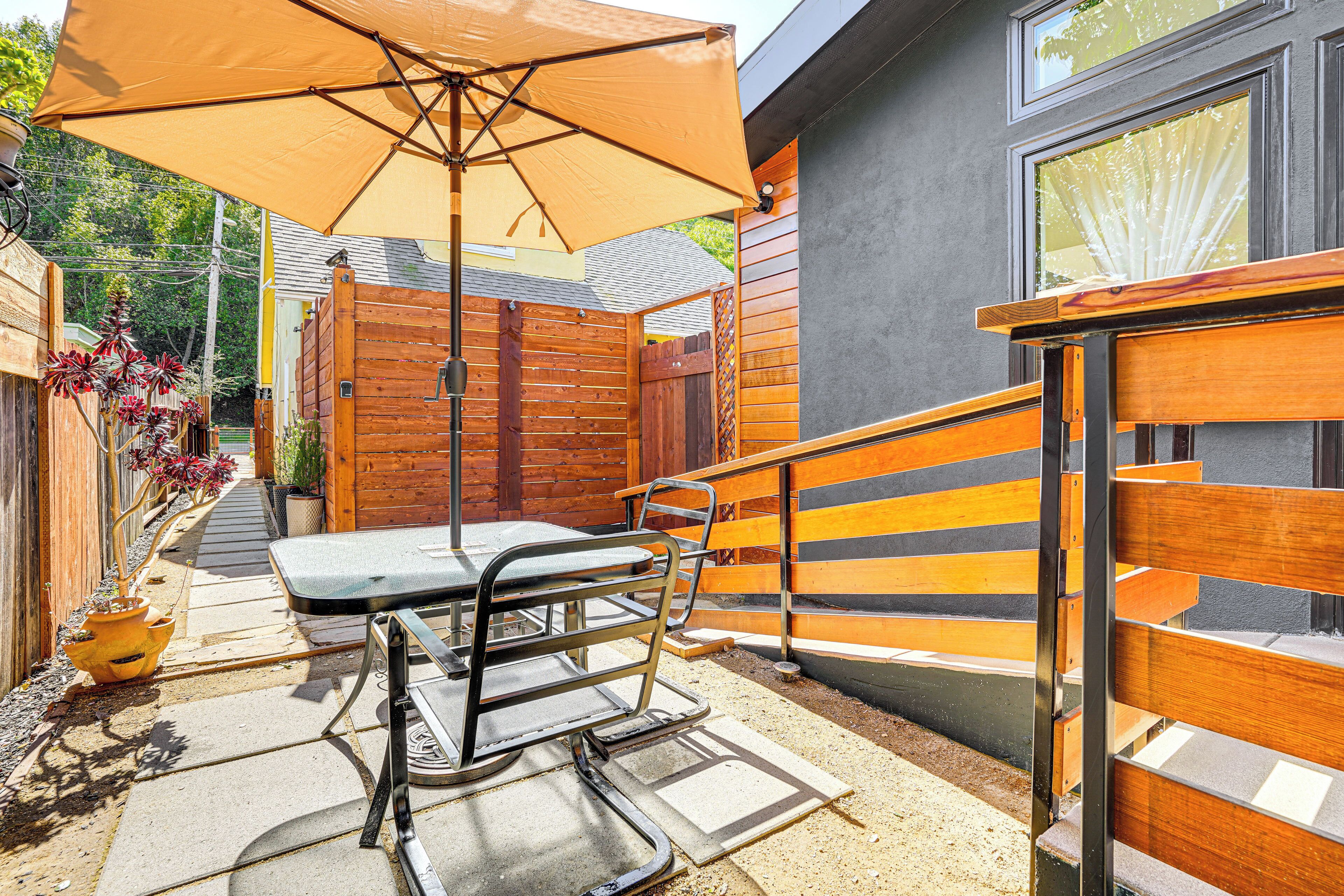 Un patio exterior con mesa y sillas, una cerca de madera y un paraguas grande.