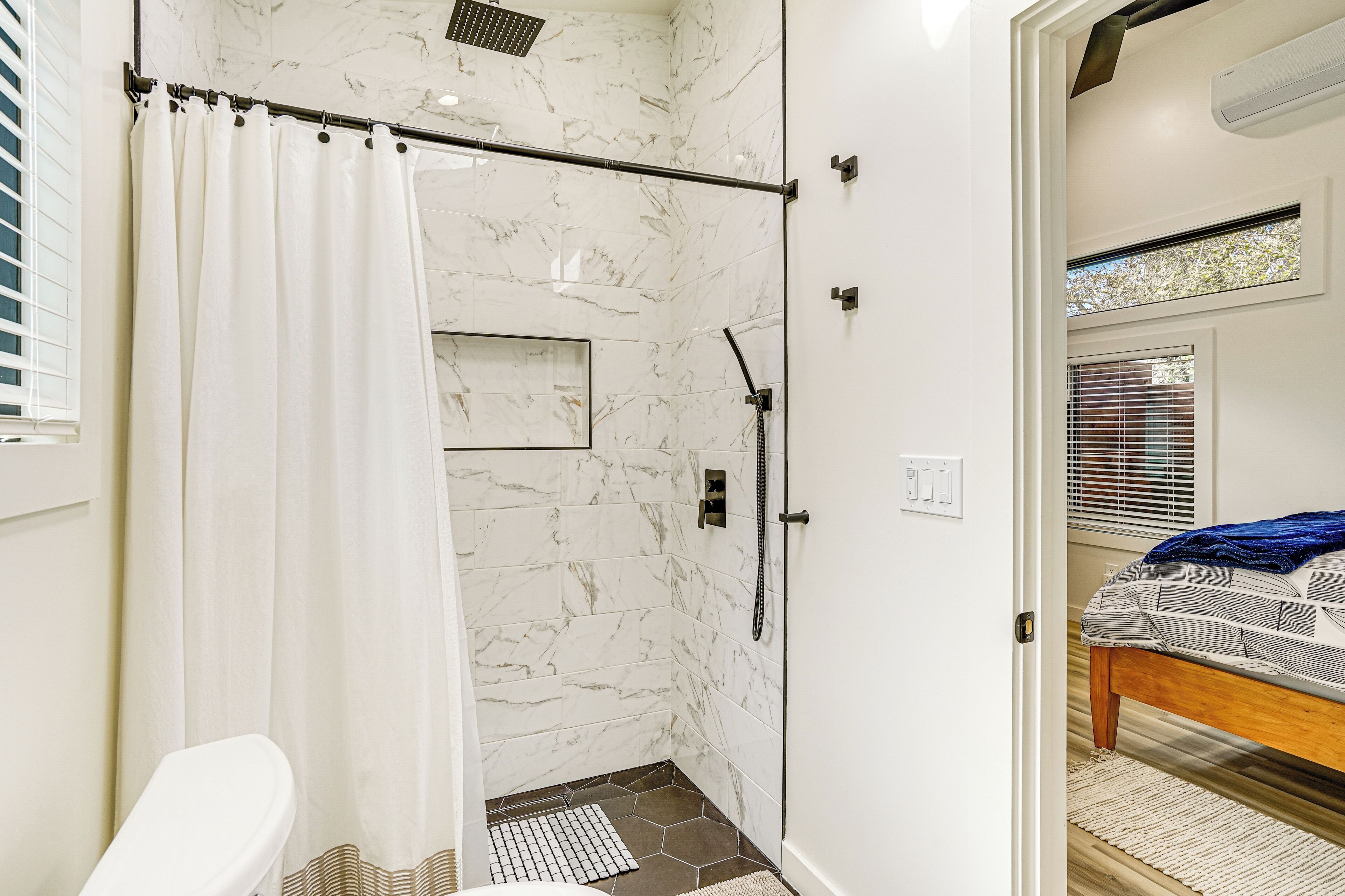 Une salle de bain moderne équipée d’une douche et de toilettes, et une chambre visible avec un lit et une fenêtre.