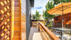 Una zona patio con ringhiere in legno, un tavolo con sedie e un ombrellone grande.