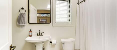 A bathroom with a white sink, mirror, toilet, and a shower curtain.