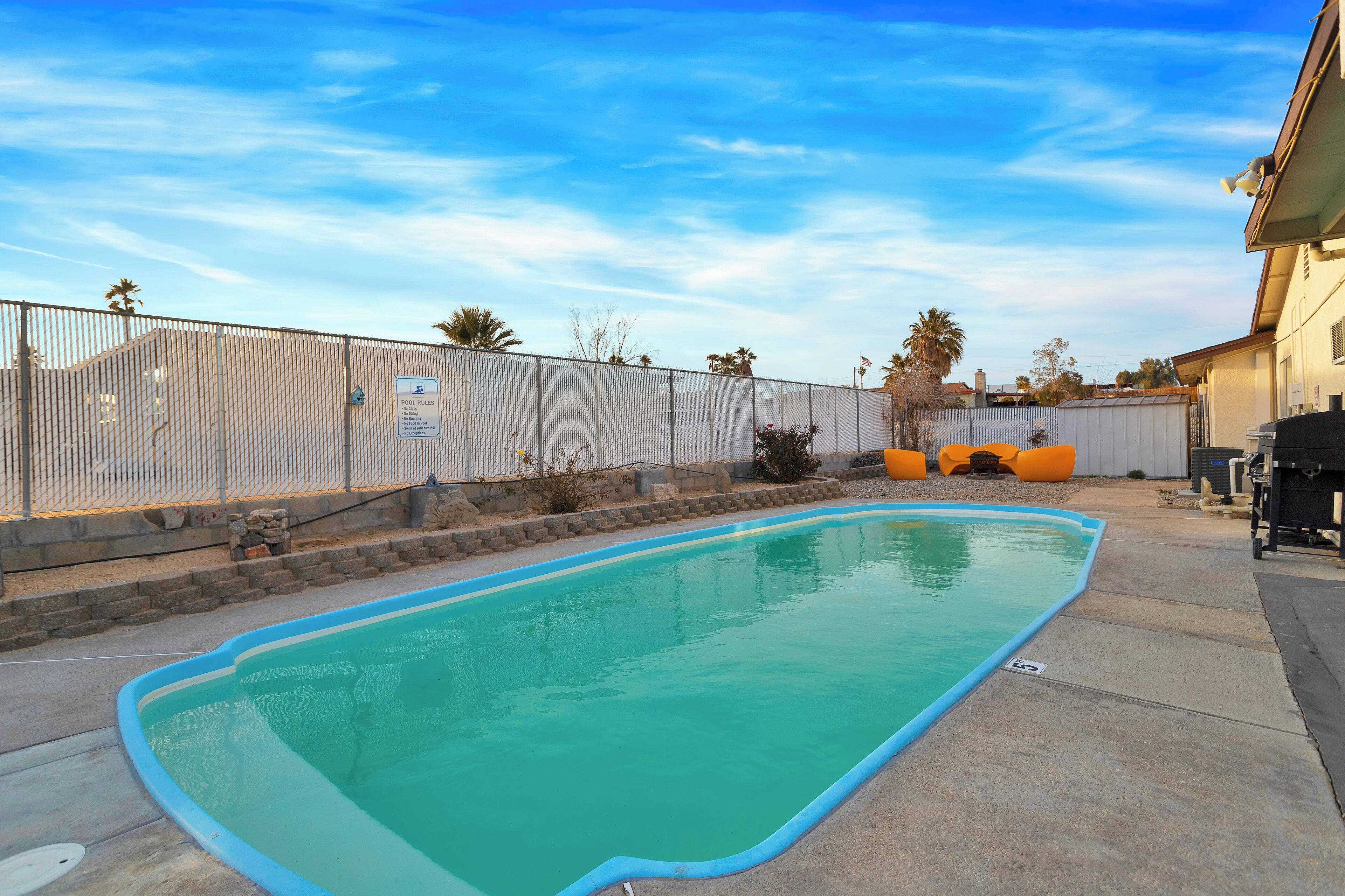 A swimming pool with a blue edge, surrounded by a fence and a stone wall.