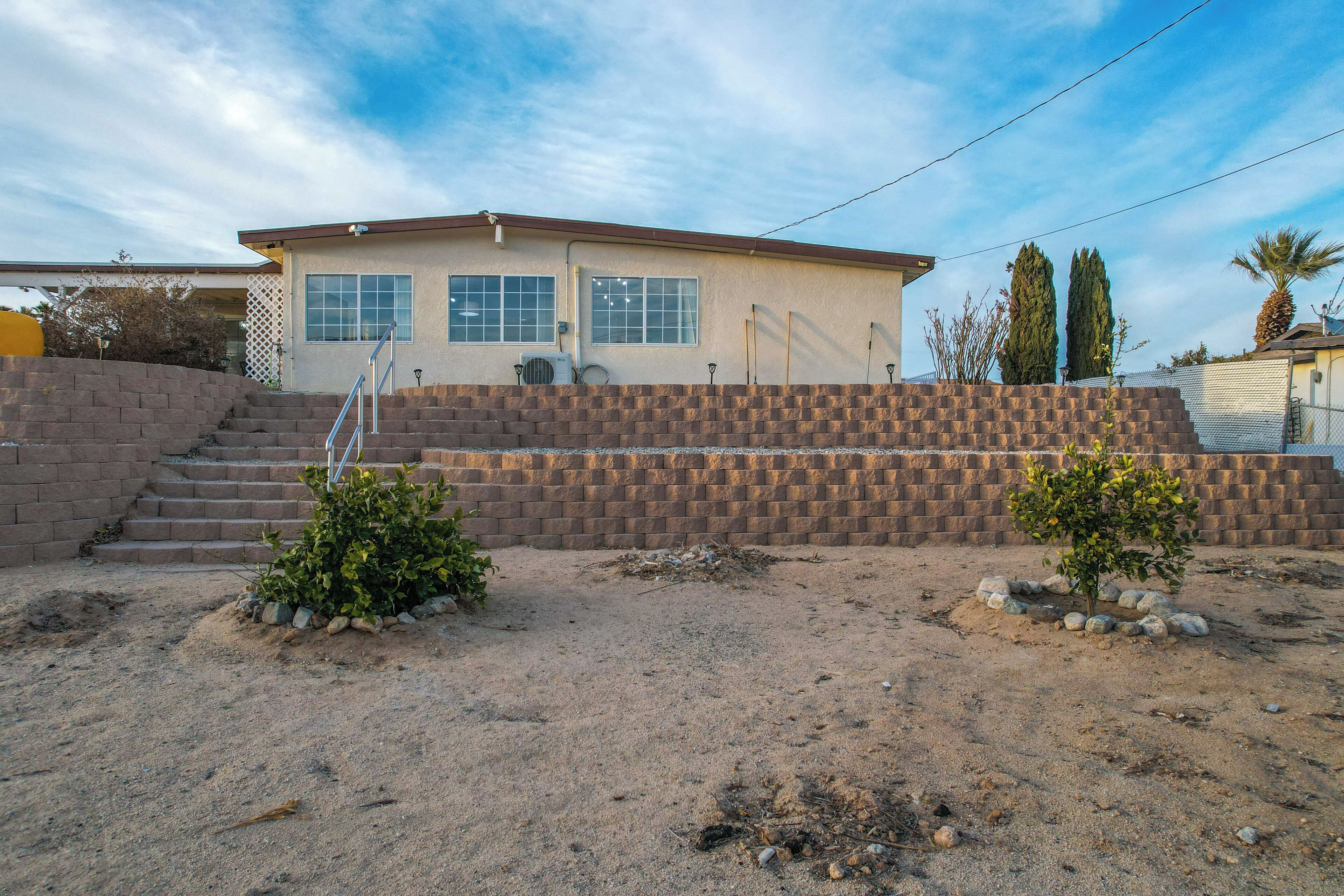 A single-story house with a brick exterior, a small front yard with a few plants, and a clear sky.