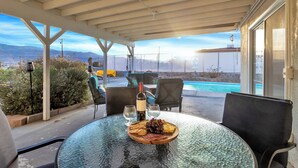 A covered outdoor seating area with a table set for two, featuring a plate of cheese and grapes, a bottle of wine, and two glasses. - 6 Mi to Joshua Tree: Home w/ Outdoor Oasis & View! (Twentynine Palms)